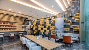 A modern lounge area with a long wooden table, multiple seating options, and a wall of bookshelves. - Atour Hotel Daguanyuan Jinan (Jinan)