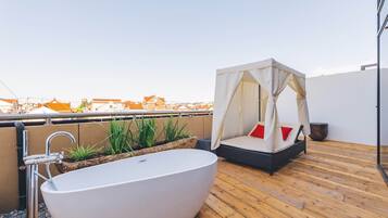 A rooftop terrace with a large freestanding bathtub, a cushioned seating area with a canopy, and a view of the cityscape.