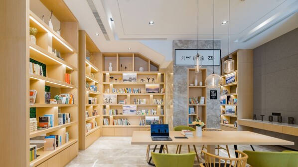 Una biblioteca moderna con estanterías de madera, una mesa central con una computadora portátil y sillas verdes.