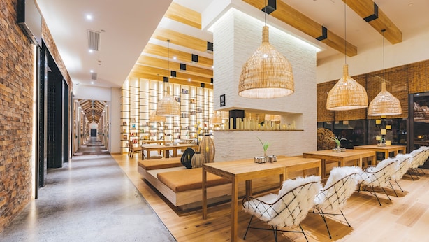 A modern interior with a long hallway leading to a seating area with tables and chairs, wooden beams on the ceiling, and a brick wall on one side. - Atour Hotel Mulan Pishang Building Wuhan (Wuhan)