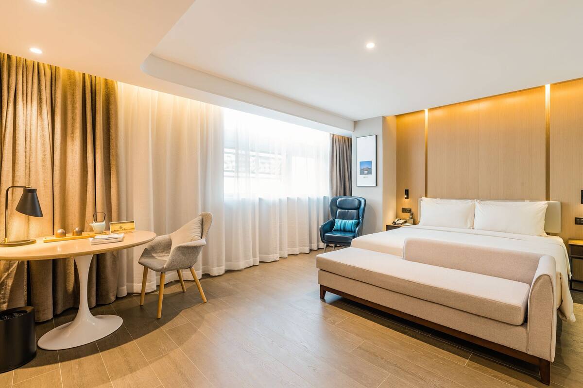 Ein Hotelzimmer mit einem Bett, einem Schreibtisch, einem Stuhl und einem großen Fenster.