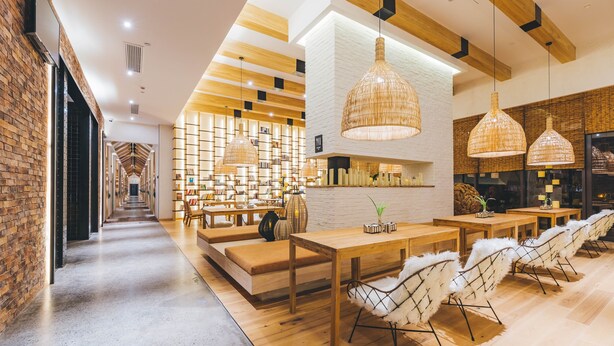 A modern interior with a long hallway leading to a seating area with tables and chairs, wooden beams on the ceiling, and a brick wall on one side. - Atour Hotel Panlong Avenue Wuhan (Wuhan)