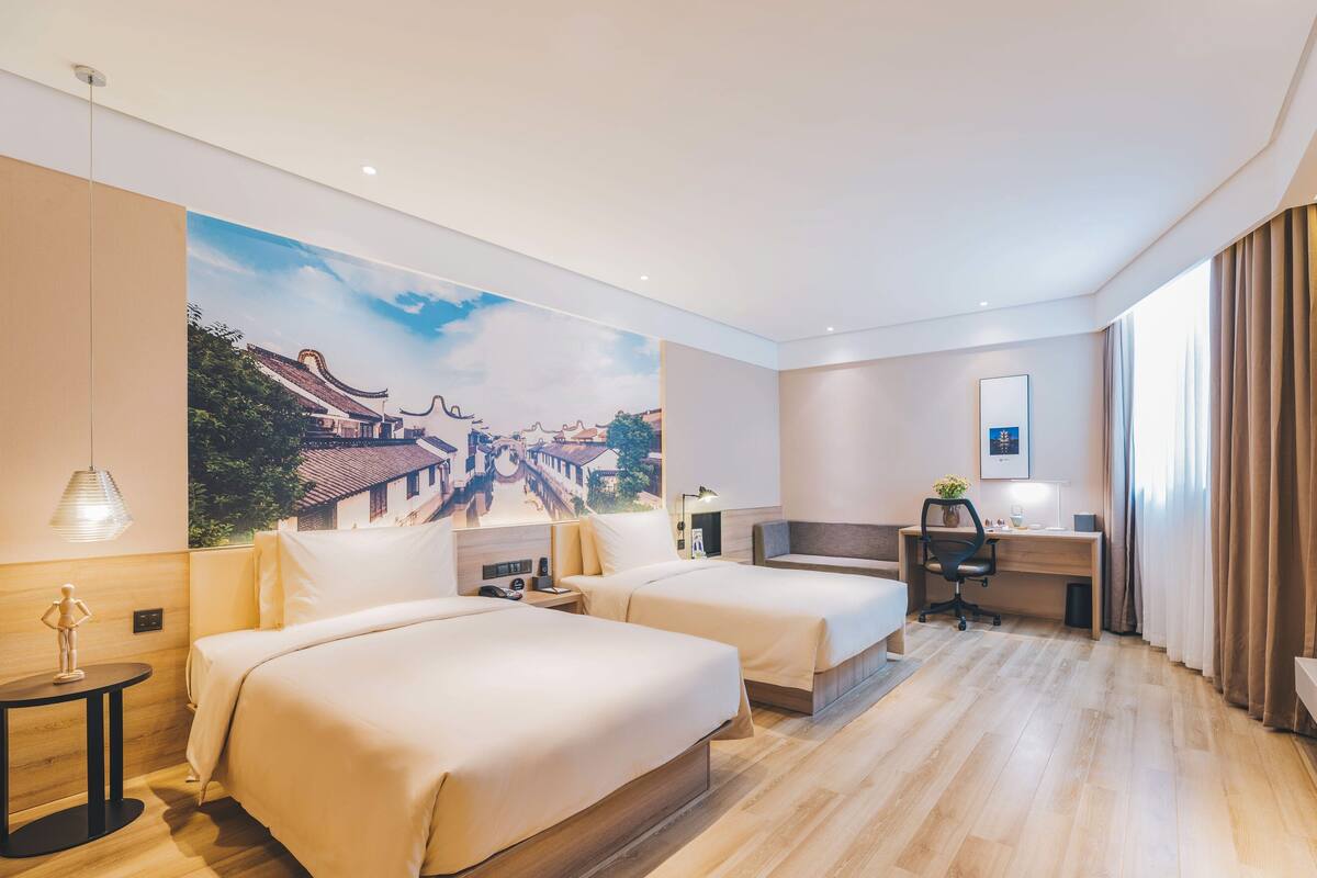 Ein Hotelzimmer mit zwei Betten, einem Schreibtisch, einem Stuhl, einer Lampe und einem großen Wandbild.