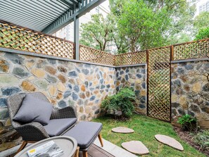 A stone wall with a bamboo lattice fence, outdoor seating with cushions, and a small garden area with stepping stones. - Atour Hotel Changhong North Road Xiangyang (Xiangyang)