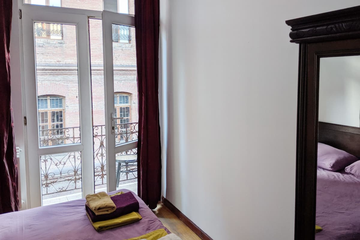 A hotel room with a bed, a window with curtains, and a view of a brick building.