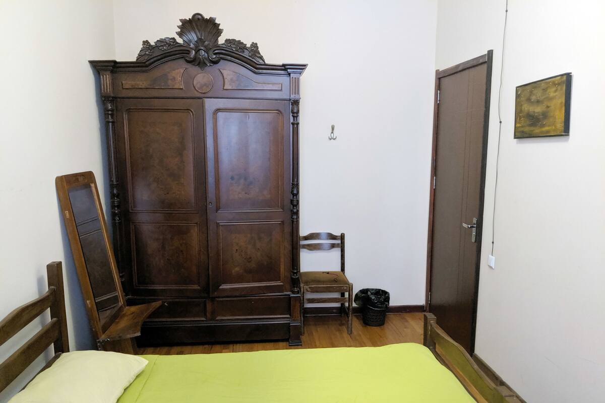 A room with a bed, a wooden wardrobe, a chair, and a door.