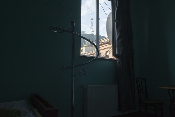 A room with a window overlooking a building, a radiator, a chair, and a bed.