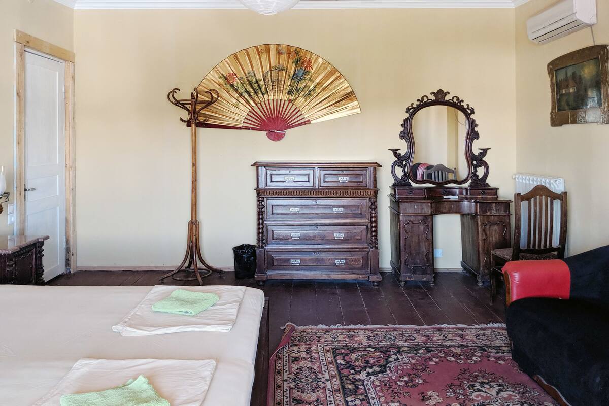 A bedroom with a bed, a wooden dresser, a mirror, a floor lamp, and a red chair.