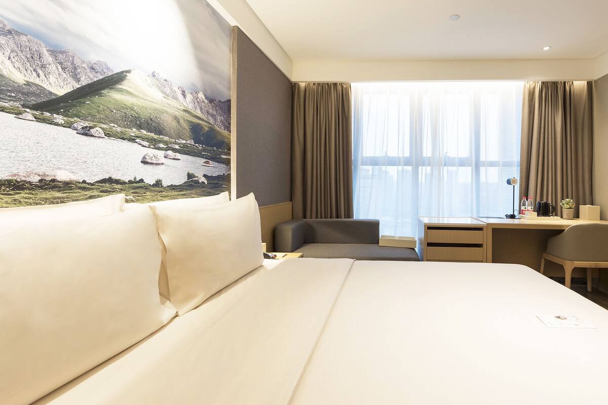 A hotel room with a large bed, a desk, a chair, and a view of mountains and a lake.