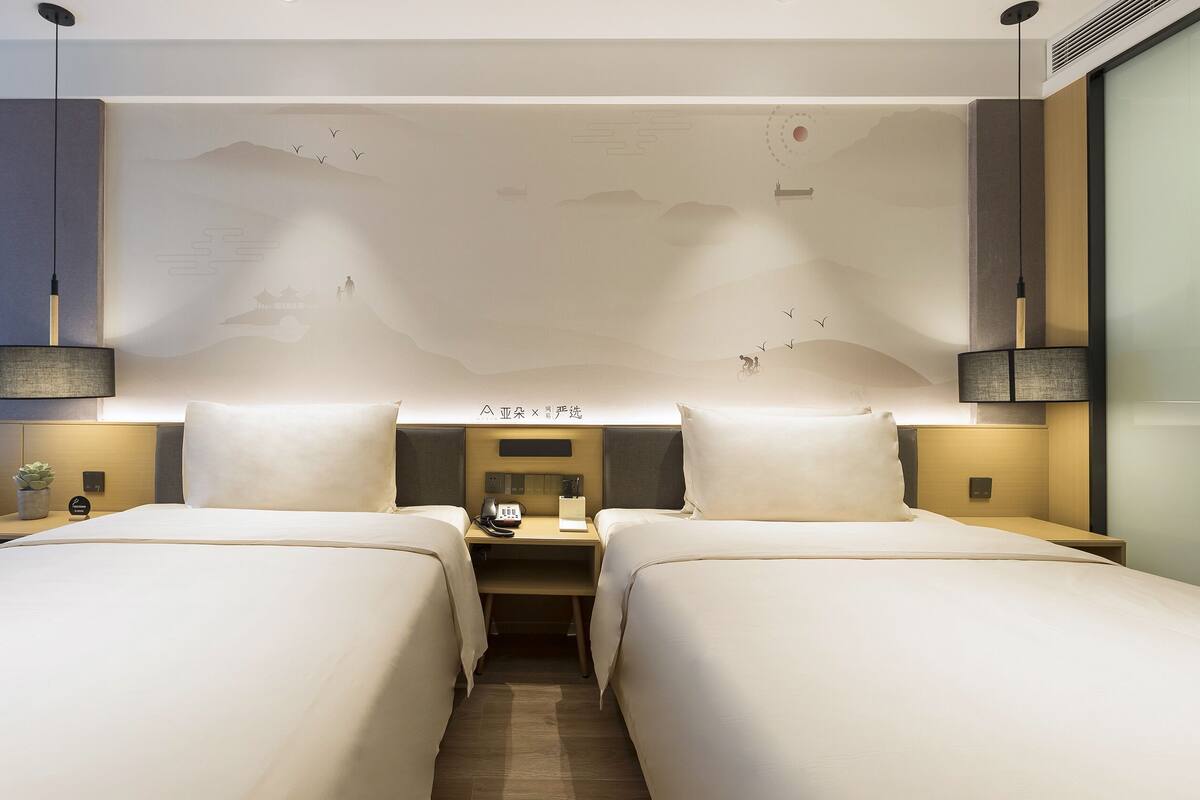 A hotel room with two beds, a nightstand with a phone, a lamp, and a wall with a mountain design.