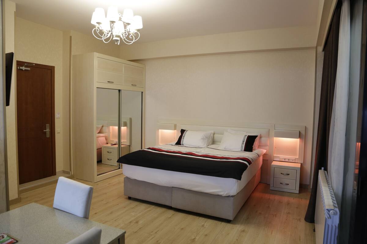 A bedroom with a bed, bedside tables, a mirror, a wardrobe, and a chandelier.
