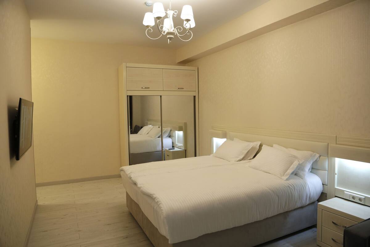 A bedroom with a bed, nightstands, a mirror, and a chandelier.