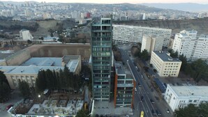 Un immeuble moderne de grande hauteur, doté d’une façade en verre, entouré d’autres immeubles résidentiels et commerciaux.