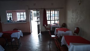 A dining area with tables covered in white tablecloths and red runners, chairs, and a view through a window. - Gee -Thorn Hotel (Chaka)