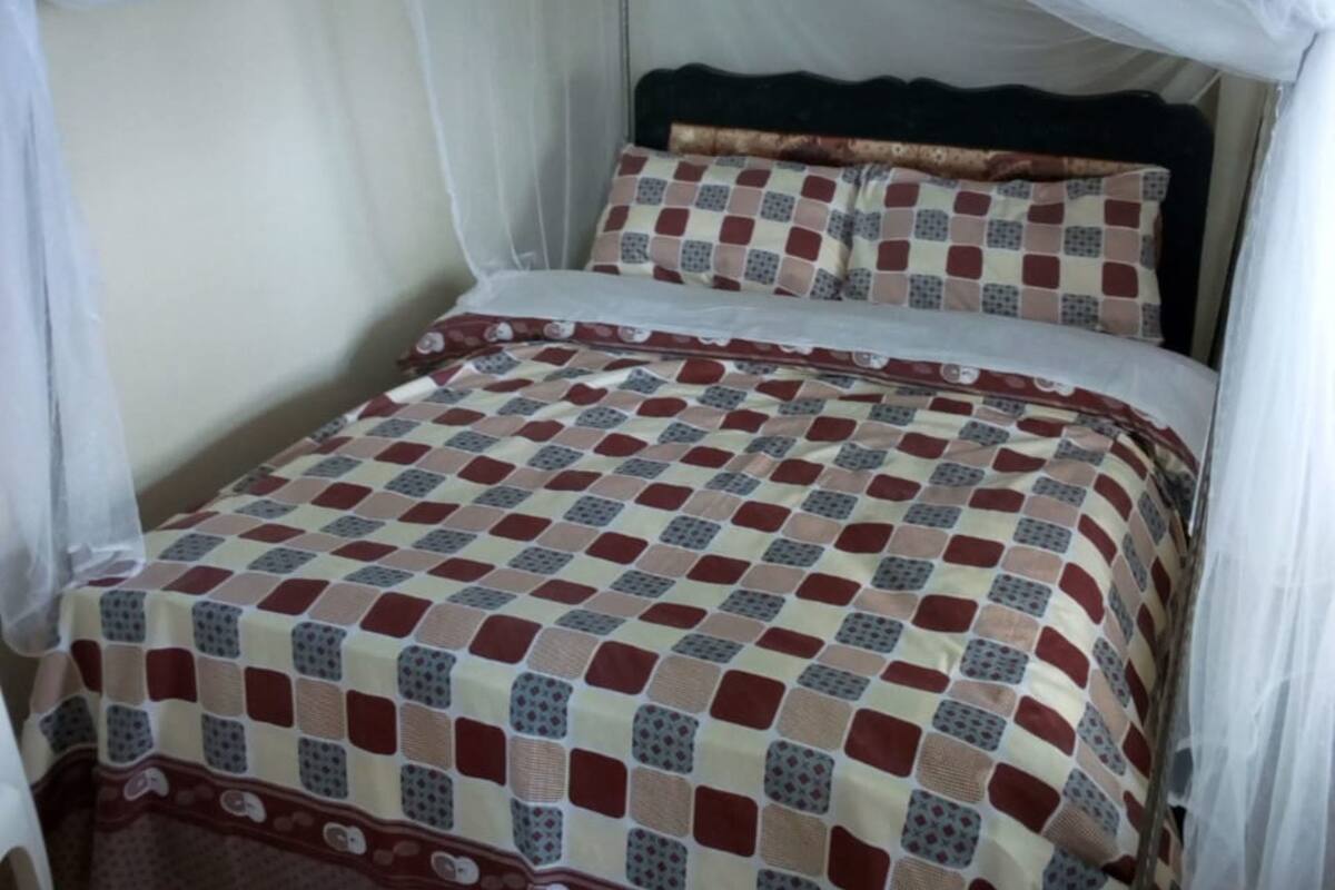 Ein Bett mit karierter Bettdecke, einem Baldachin und einem Kissen mit geometrischem Muster.