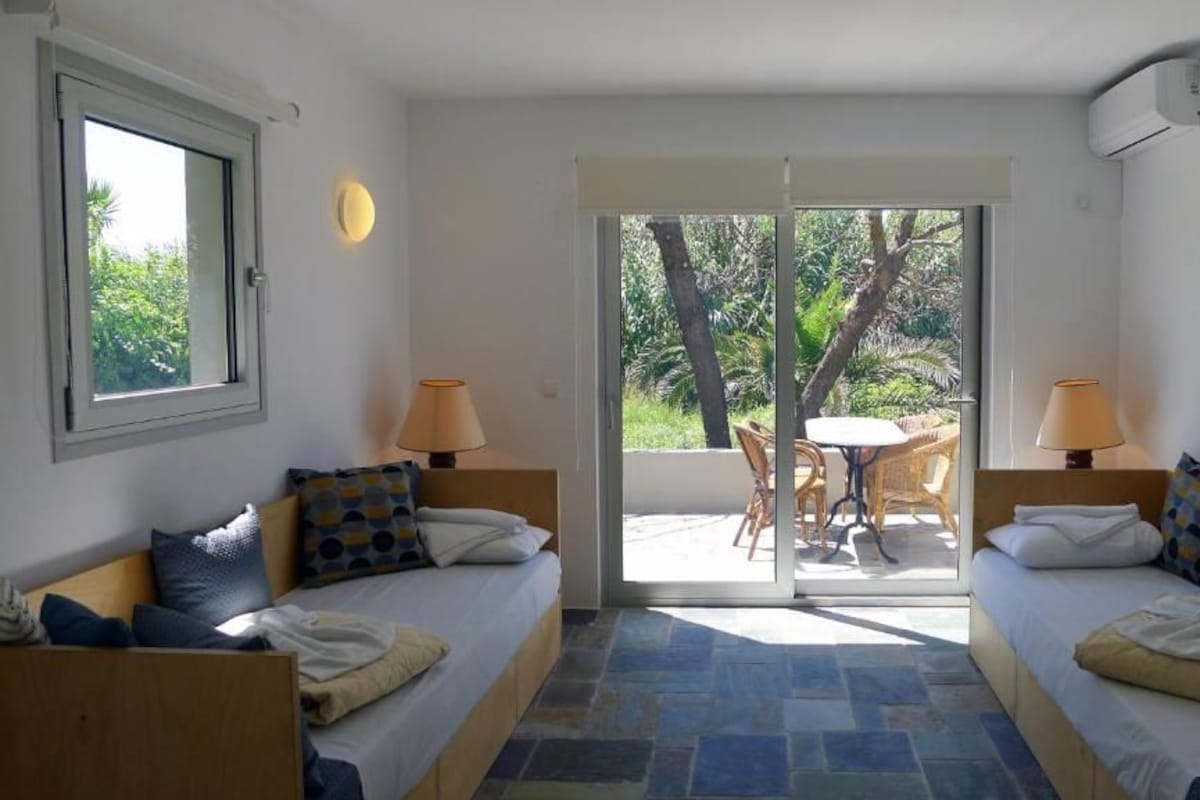 A room with two beds, a table, chairs, and a sliding glass door leading to an outdoor area.