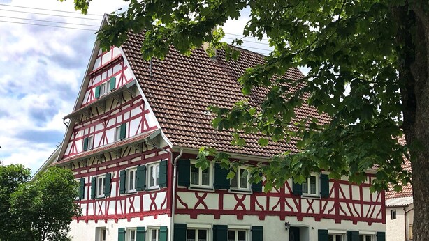 Une maison traditionnelle à colombages, dotée d’un toit à forte pente, de nombreuses fenêtres avec volets et d’un jardin bien entretenu à l’avant.