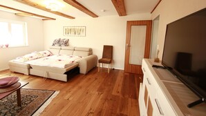 Une chambre avec un lit, une chaise, une télévision, des poutres en bois et une fenêtre.