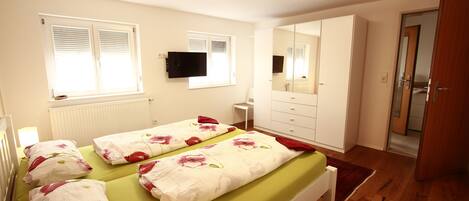 A bedroom with two beds, a mirror, a TV, and a wardrobe.