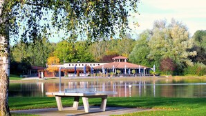 Un parc au bord du lac, avec une table de pique-nique, un bâtiment doté d’un toit rouge et des arbres en arrière-plan.