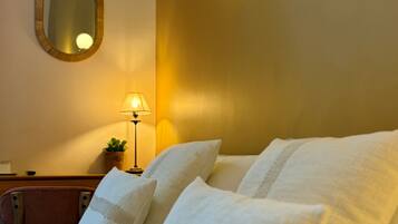 A neatly made bed with white linens and pillows, a round mirror on the wall, and a wall-mounted light fixture.