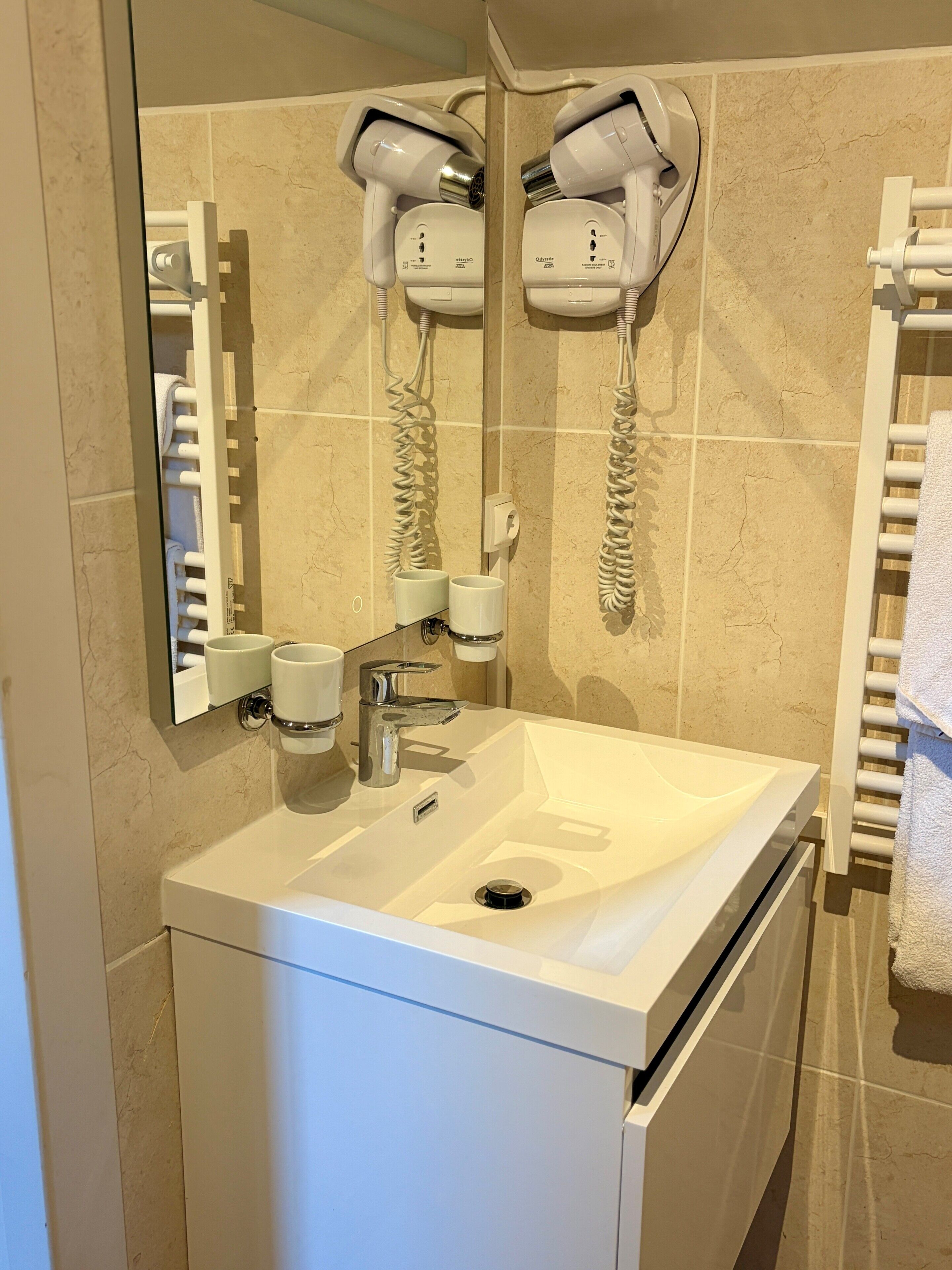 Un baño con lavamanos blanco, espejo, secador de pelo y toallero.