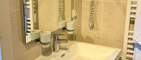 Un baño con lavamanos blanco, espejo, secador de pelo y toallero.