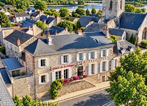 Un edificio de piedra con un letrero que dice 'Hotel de la Soigne' en un entorno urbano, con un río e iglesia al fondo.