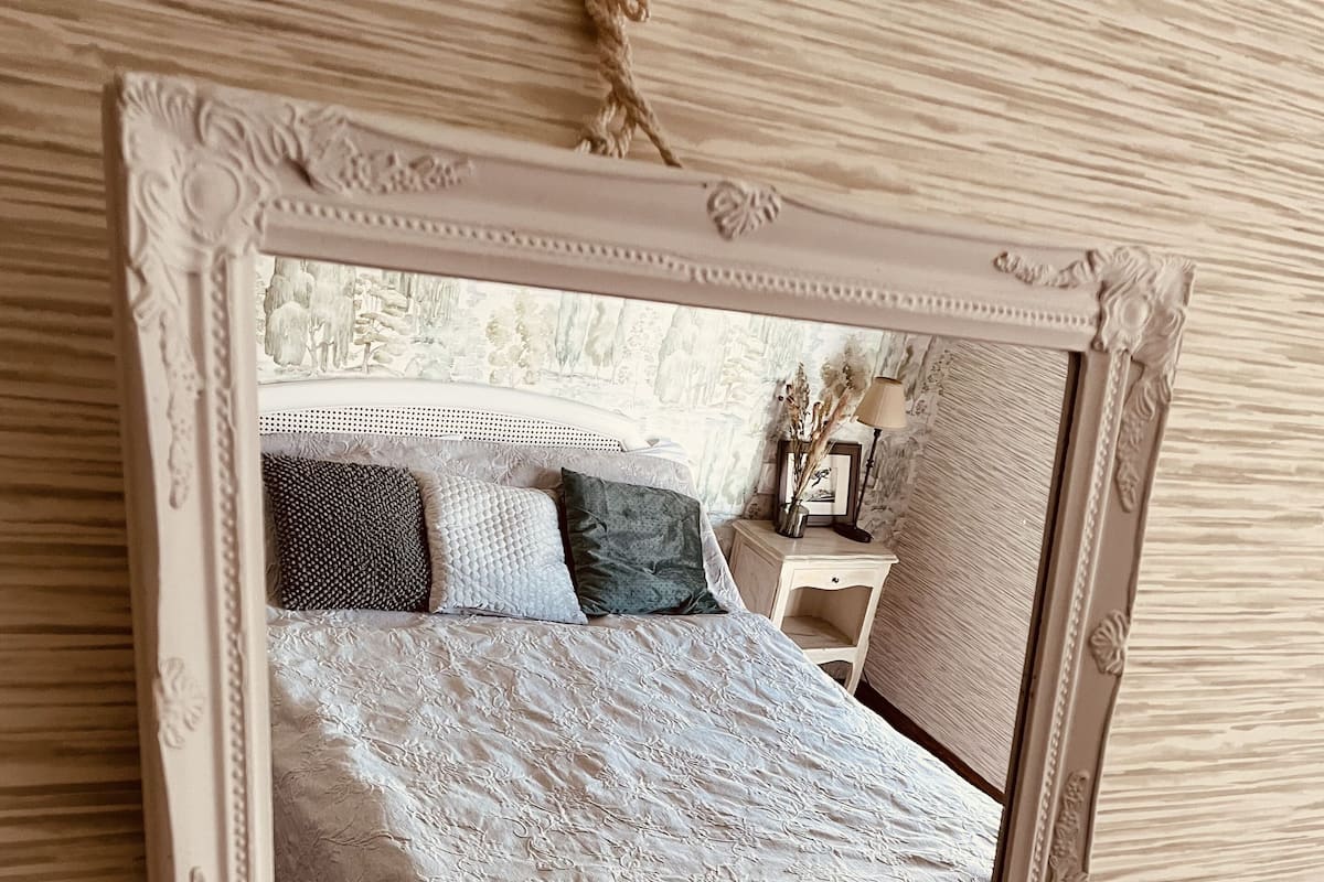 A bedroom with a bed, pillows, a nightstand, and a mirror.