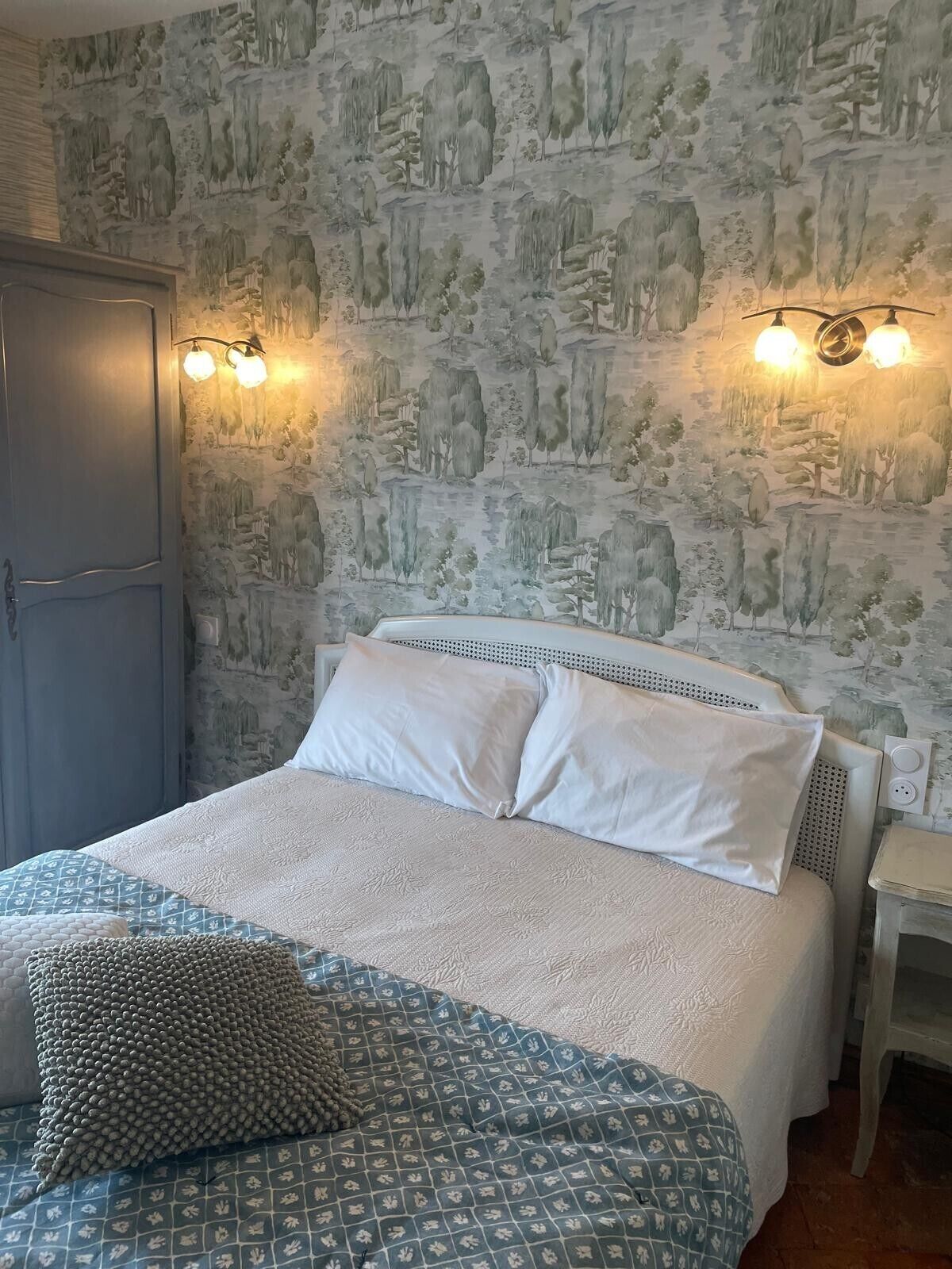 A bedroom with a bed, pillows, a bedside table, and a wall with a nature-themed wallpaper.