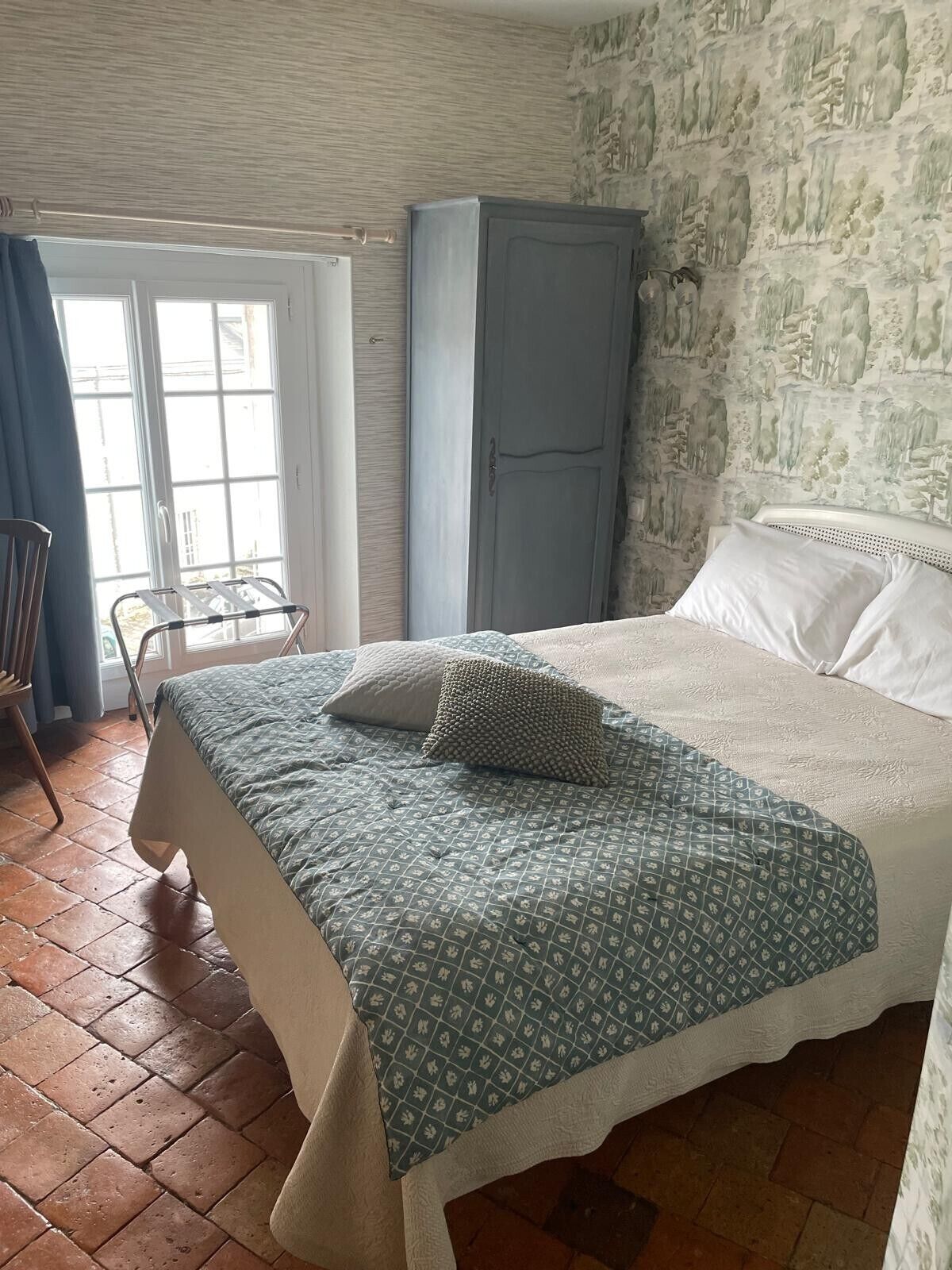 A bedroom with a bed, a chair, a wardrobe, and a window.