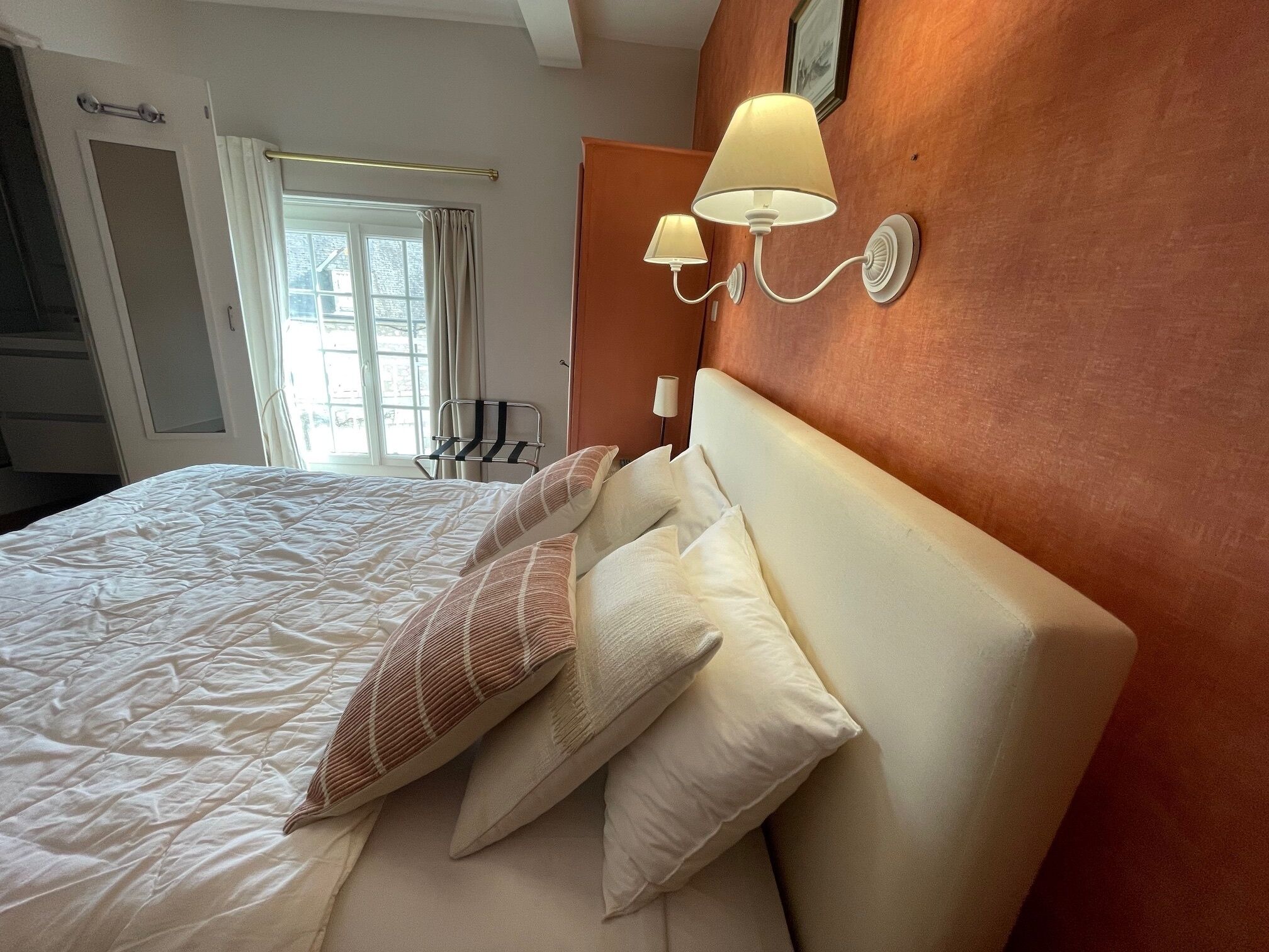 Een hotelkamer met een bed, twee wandlampen, een raam met gordijnen en een deur.