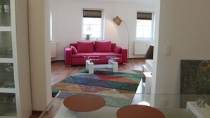 A living room with a red sofa, a coffee table, and a patterned rug. - Ferienwohnung Lilie (Lübbenau/Spreewald)