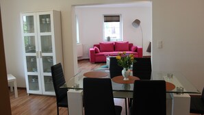 A modern living room with a glass dining table, black chairs, a pink sofa, and a white cabinet with glass doors. - Ferienwohnung Lilie (Lübbenau/Spreewald)