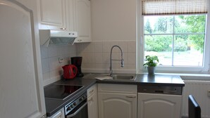 A kitchen with white cabinets, a black countertop, a stainless steel range, a dishwasher, and a window with a view of greenery. - Ferienwohnung Lilie (Lübbenau/Spreewald)