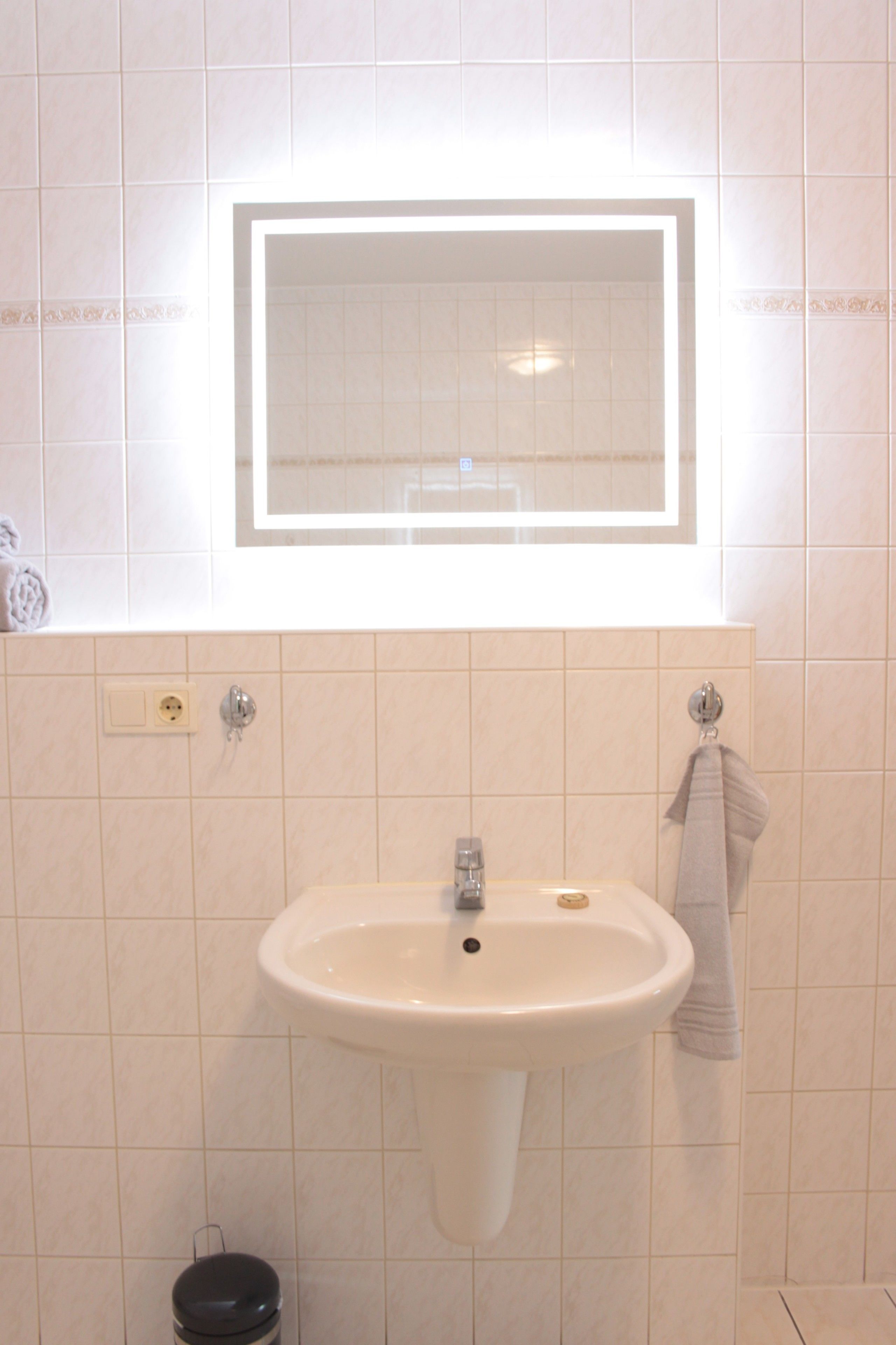 Een badkamer met een witte wastafel, een spiegel erboven en een handdoek aan de muur.