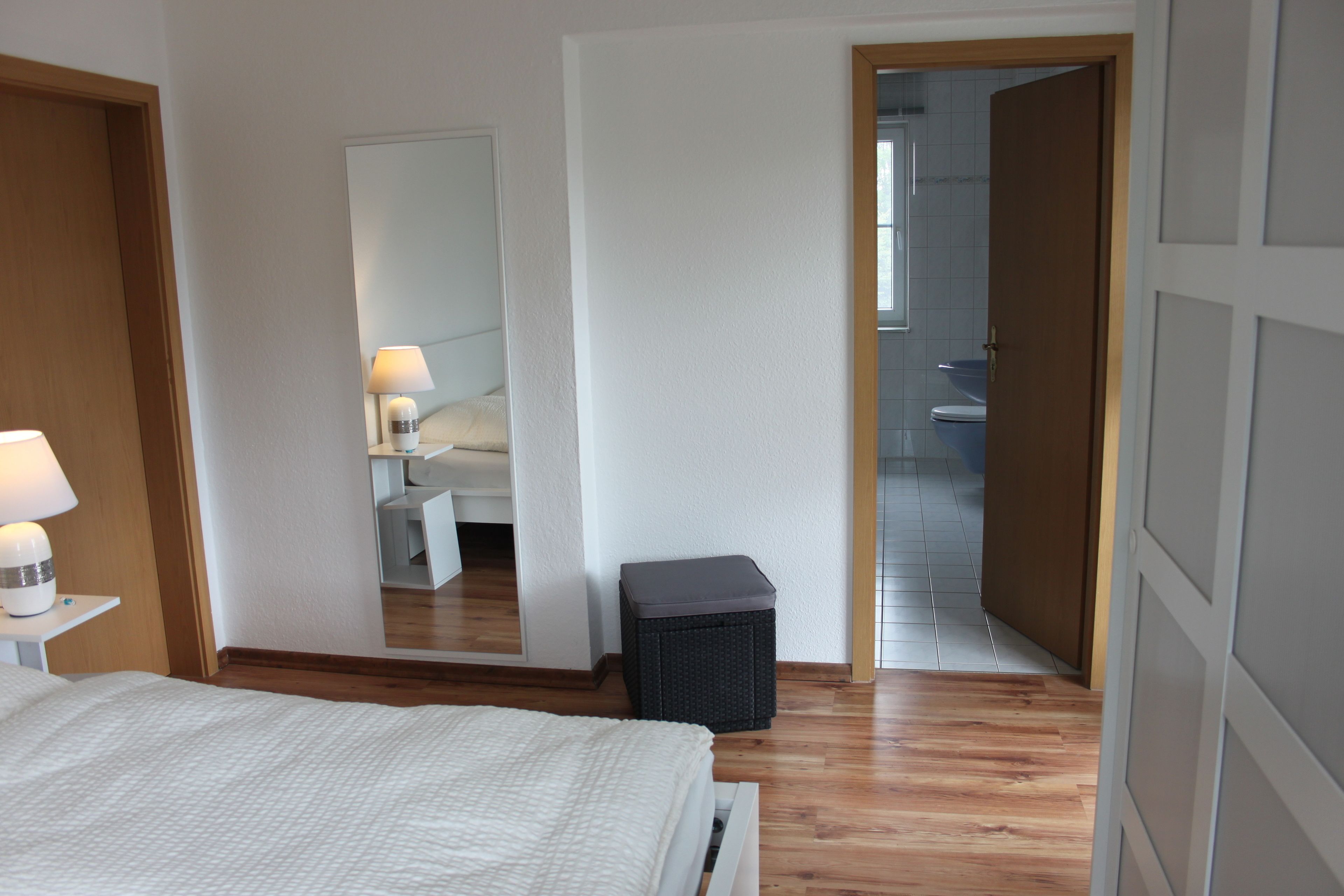 A bedroom with a bed, bedside lamp, and a small trash bin.