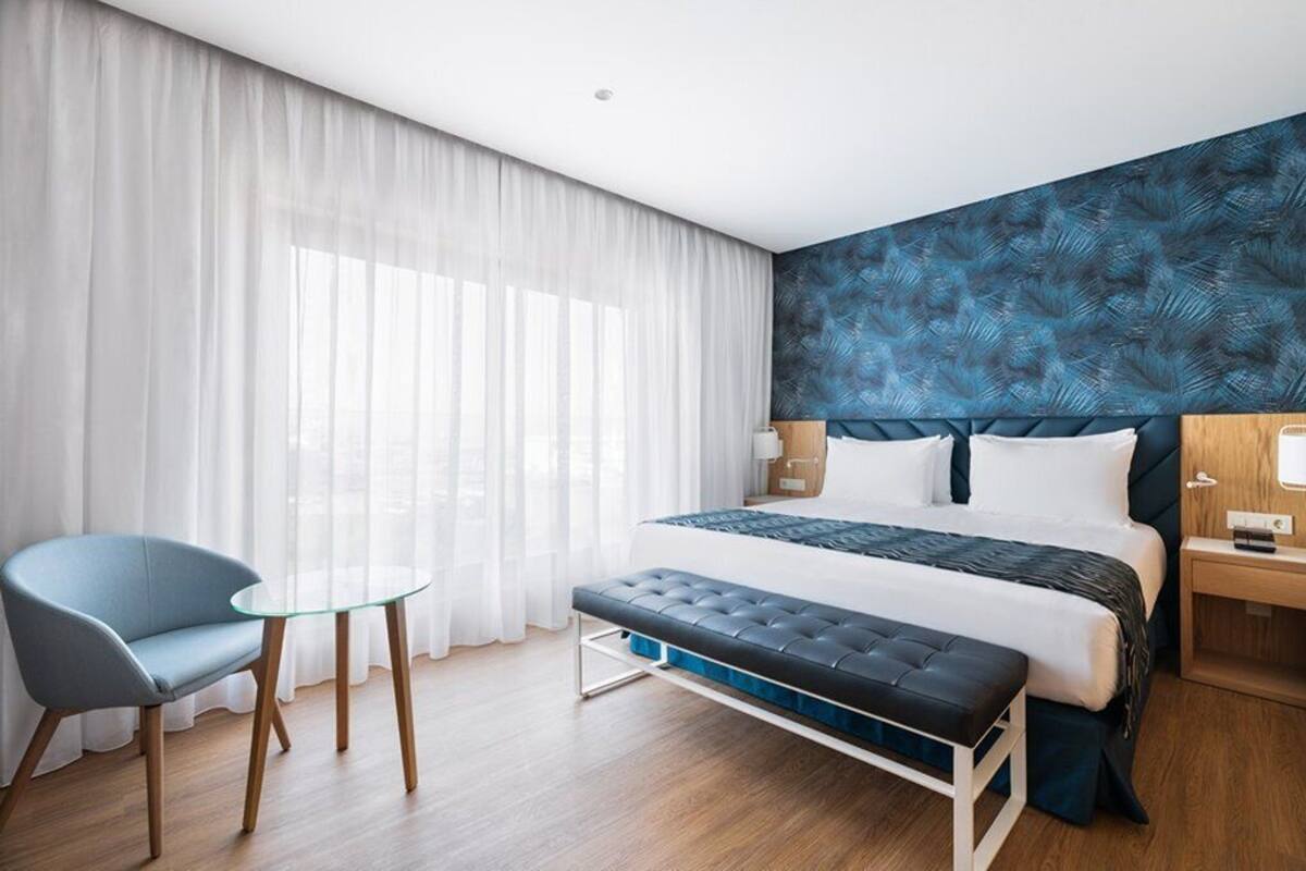 Een hotelkamer met een bed, een stoel, een klein tafeltje en een nachtkastje.