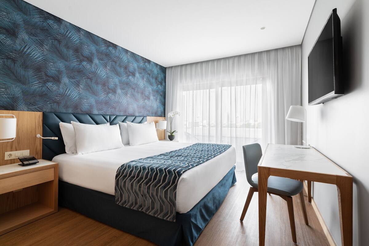 Een moderne hotelkamer met een groot bed, een bureau, een stoel, een televisie en een raam met gordijnen.