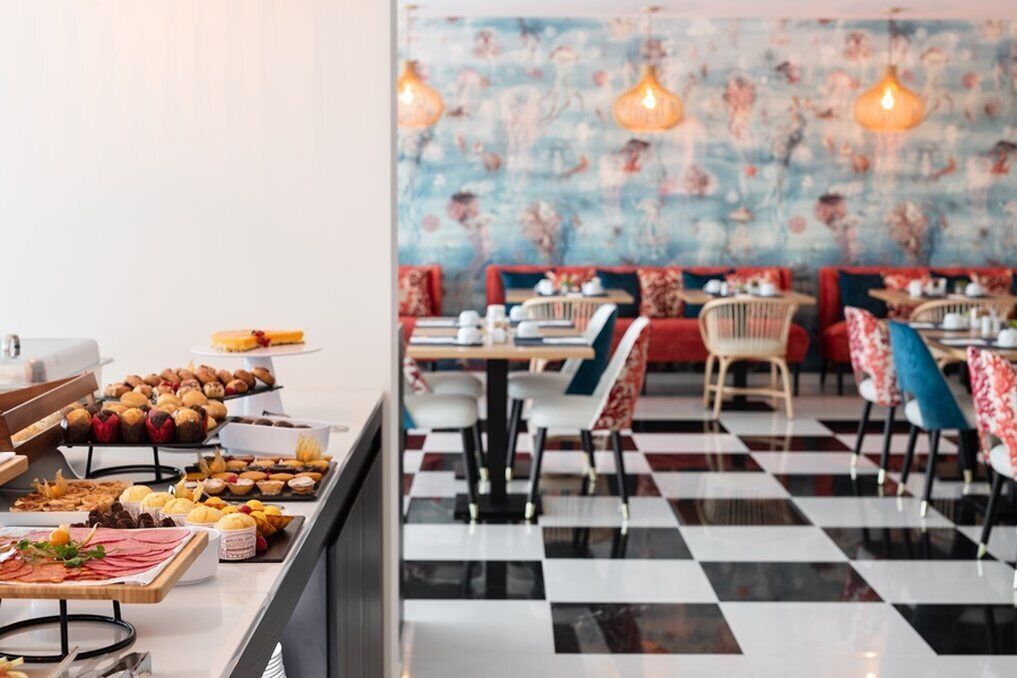 A restaurant with checkered flooring, a buffet with various food items, and red and blue upholstered chairs.