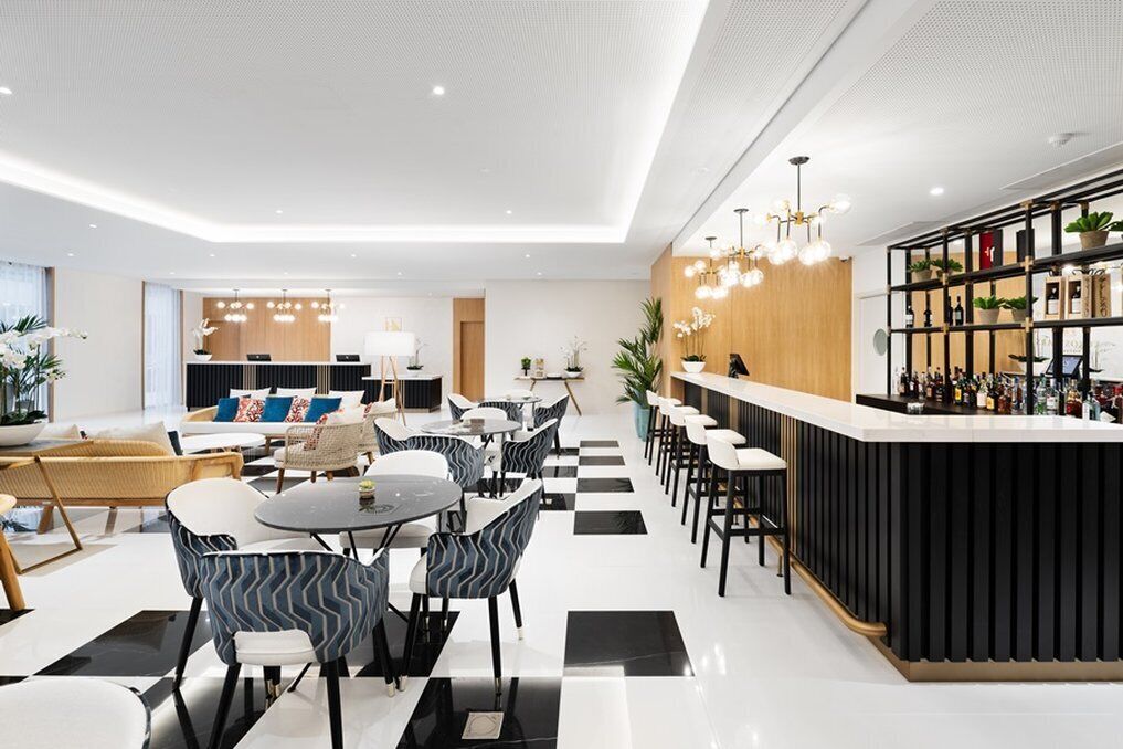 Un hall d’hôtel moderne avec un sol à carreaux, un comptoir d’accueil, des espaces salon et un bar doté d’un comptoir noir.