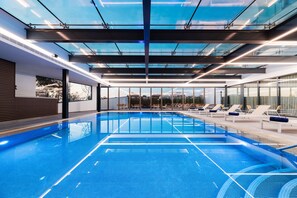 An indoor swimming pool with clear glass ceilings, lounge chairs, and a view of the cityscape. - Eurostars Matosinhos (Matosinhos)