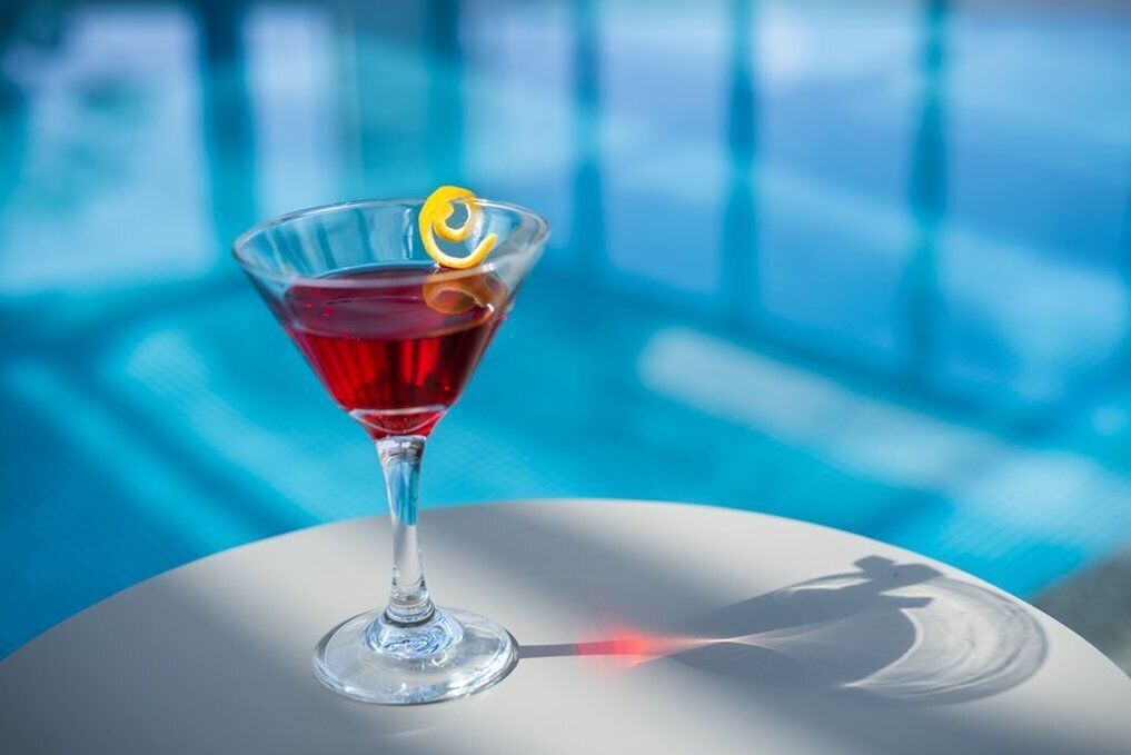 A martini glass with a lemon twist on a reflective surface.