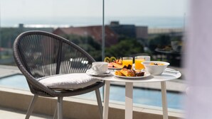 Un balcón con una silla de mimbre, una mesita con artículos de desayuno y vista a la piscina.