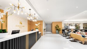 Una moderna zona de recepción de hotel con un aspecto limpio y cuidado, que incluye un mostrador de recepción, área de descanso e interior bien iluminado.