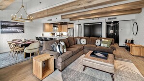 A modern living room with a sectional sofa, wooden coffee table, and a dining area with a table set for four. - A/C, Pool, Slopeside, Hot Tub, Elevator, Ski Locker, In Unit Washer/Dryer (Steamboat Springs)
