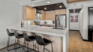 A modern kitchen with a marble island, black bar stools, wooden cabinets, and a stainless steel refrigerator. - A/C, Pool, Slopeside, Hot Tub, Elevator, Ski Locker, In Unit Washer/Dryer (Steamboat Springs)