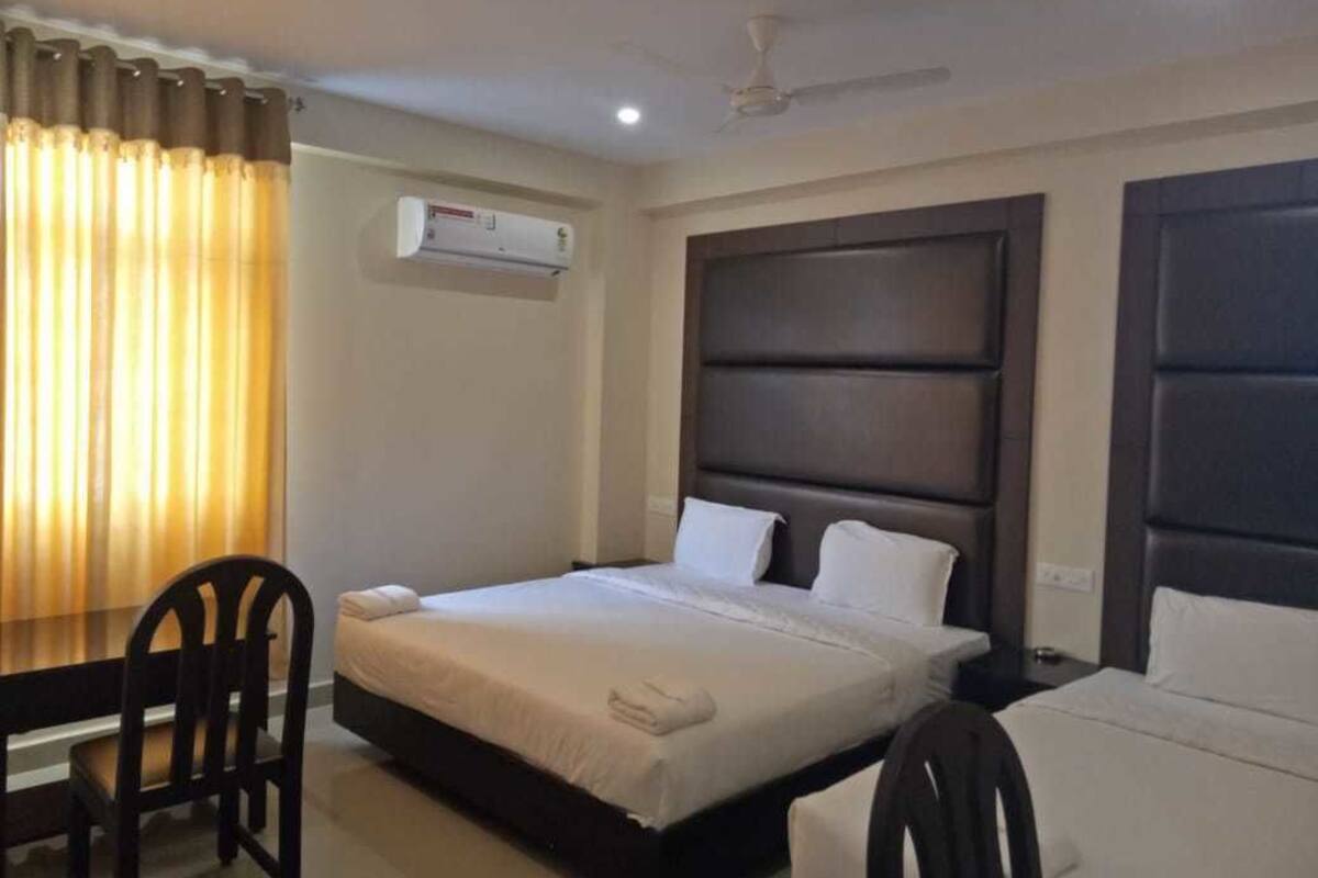 A hotel room with a bed, a desk, and a chair. There is an air conditioning unit on the wall.