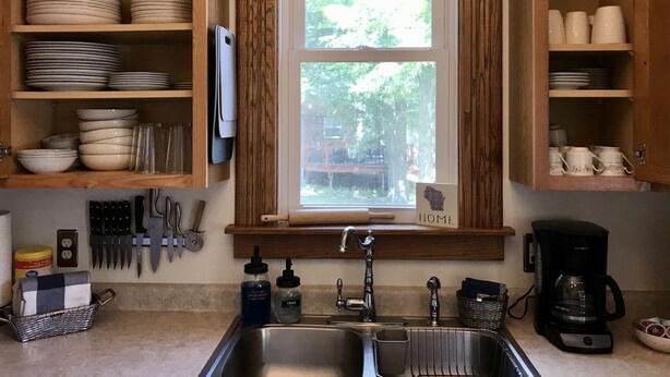 A kitchen with wooden cabinets, a window, a sink, and various kitchen utensils. - Historic 1880s Home (Osceola)