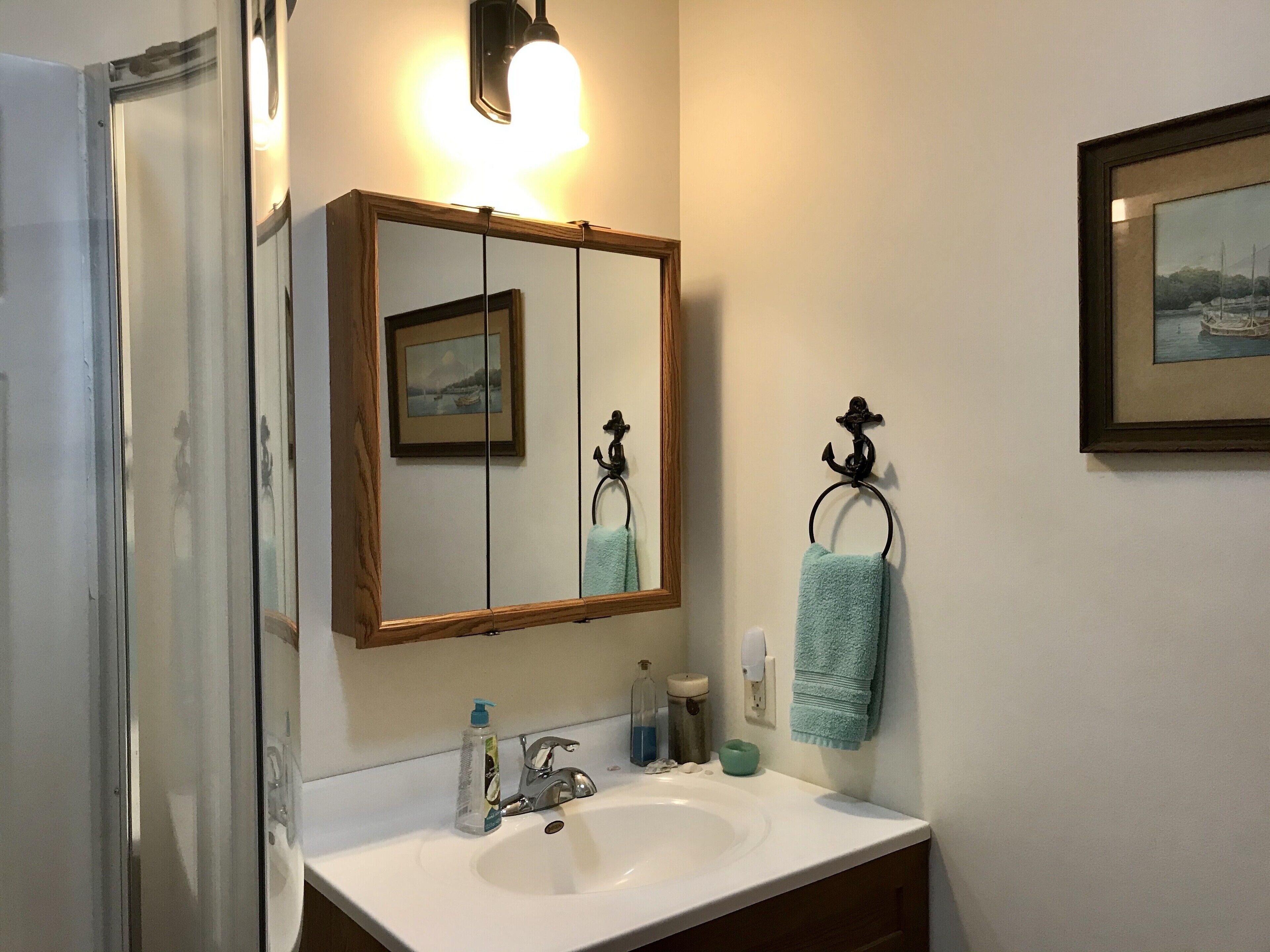 Un baño con un lavabo blanco, un espejo con marco de madera, un perchero con una toalla azul y un cuadro en la pared.
